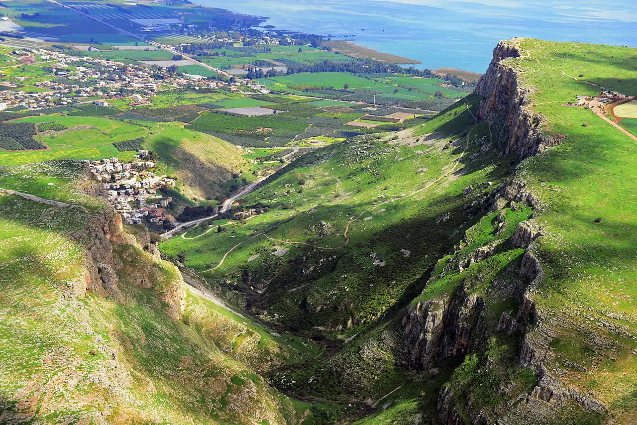 The cliff of Mount Arbel rising above green fields and the Sea of Galilee